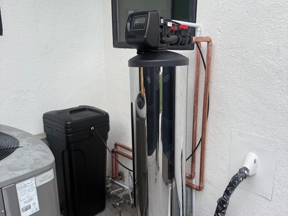 Chrome whole-house water softener installed outdoors with brine tank and copper plumbing
